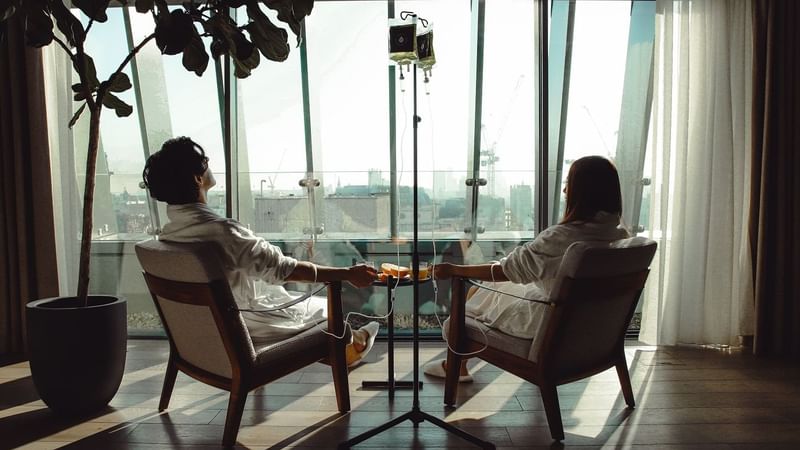 Two people in robes sitting by a window getting treatments at The Londoner Hotel