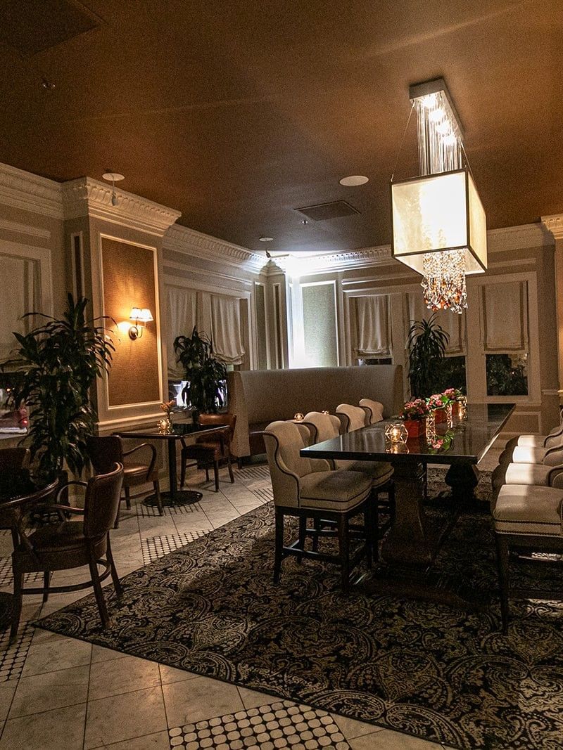 Long dining table by upholstered chairs under a glowing cube chandelier in Landmark at Warwick Melrose Dallas