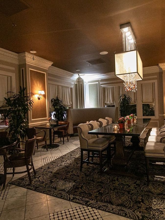 Long dining table by upholstered chairs under a glowing cube chandelier in Landmark at Warwick Melrose Dallas