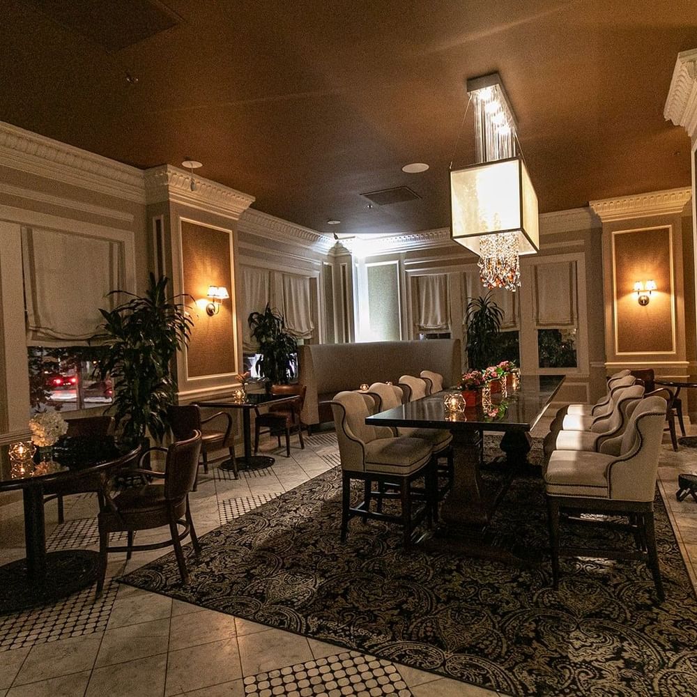 Long dining table by upholstered chairs under a glowing cube chandelier in Landmark at Warwick Melrose Dallas