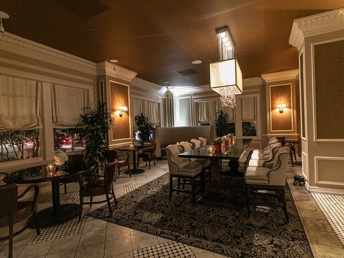 Long dining table by upholstered chairs under a glowing cube chandelier in Landmark at Warwick Melrose Dallas