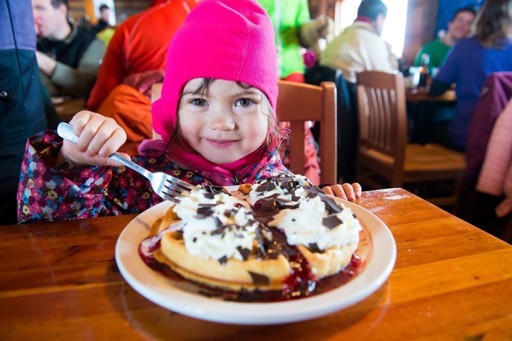 Kid having waffles with chocolate and whipped cream in Crystal Hut at Blackcomb Springs Suites