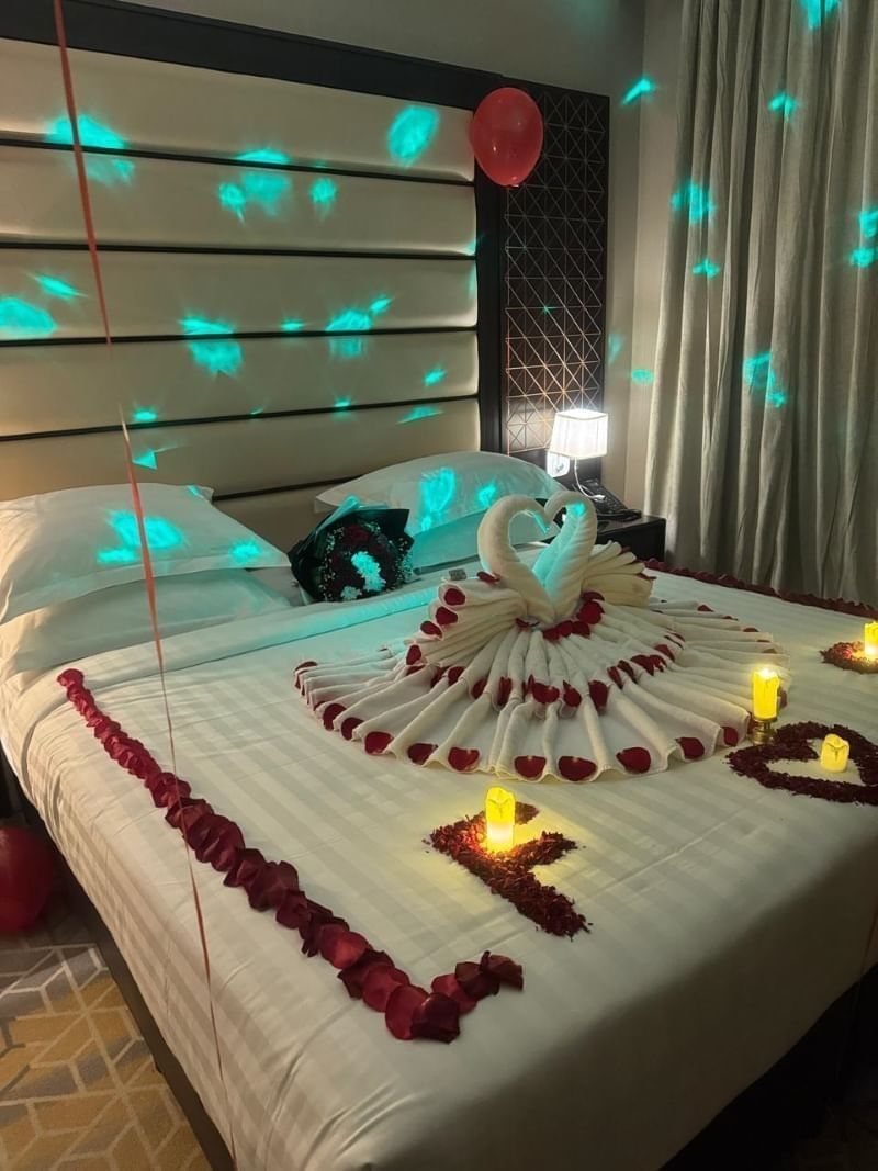 Towel swans by red rose petals under glowing party lights on a decorated bed at Naviti by Warwick Al Khobar