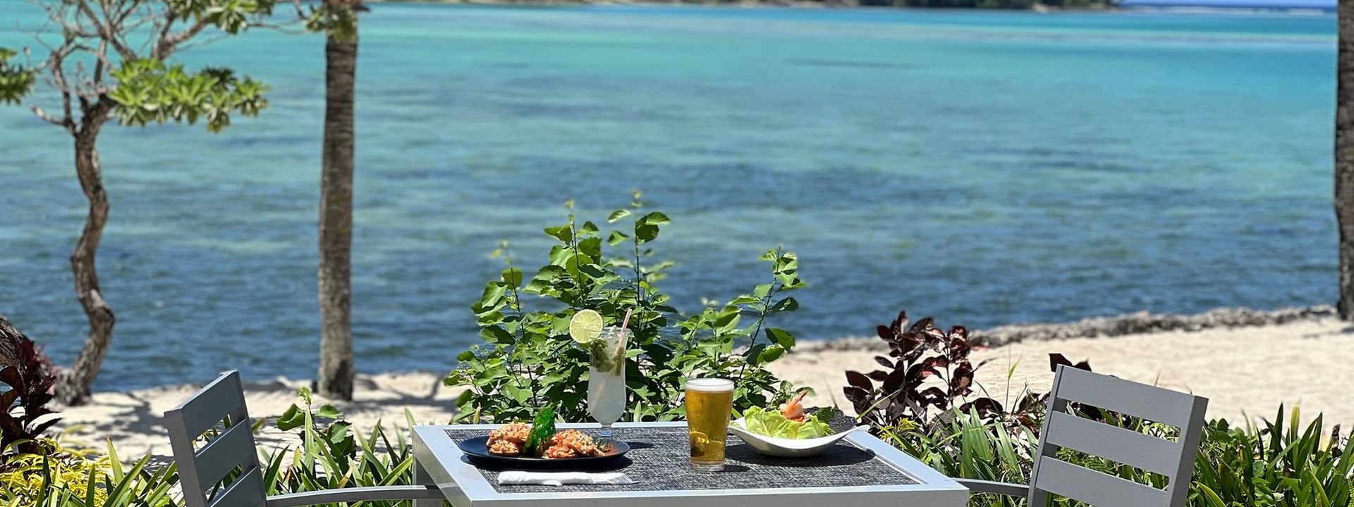 Outdoor table and chairs with food and drinks by the beach at Warwick Le Lagon - Vanuatu, Efate