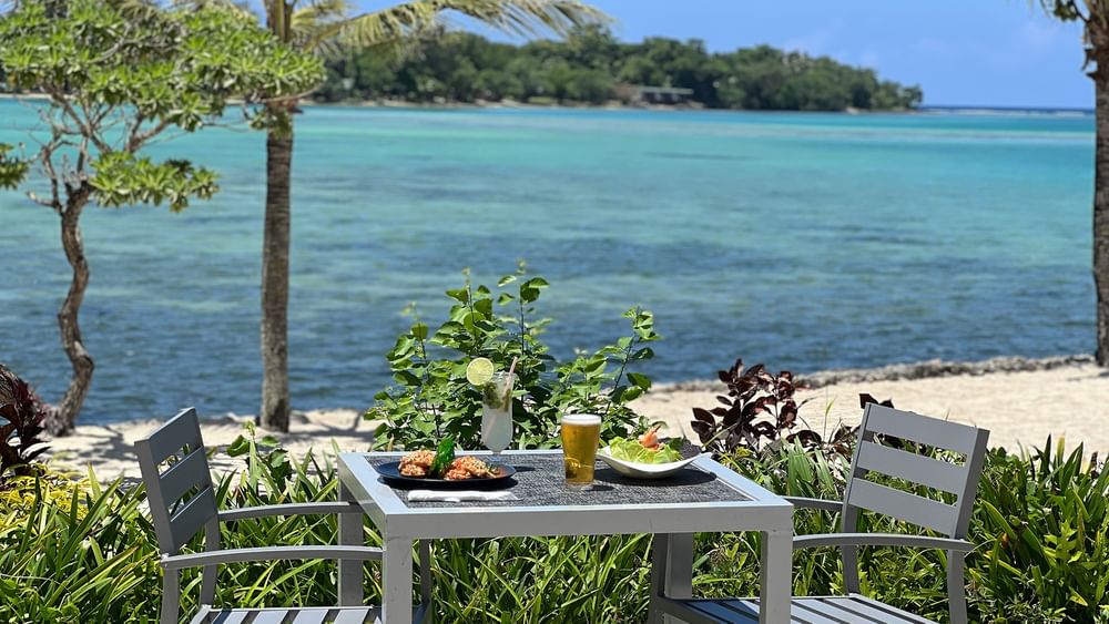 Outdoor table and chairs with food and drinks by the beach at Warwick Le Lagon - Vanuatu, Efate.