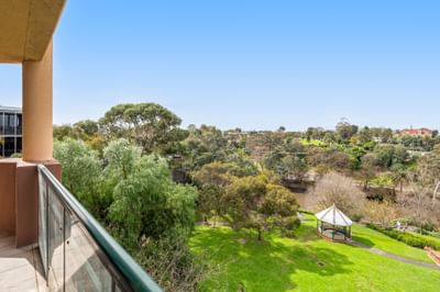 Lush green park view by a white gazebo under a clear blue sky, seen from a stone balcony at the Amora Hotel Group