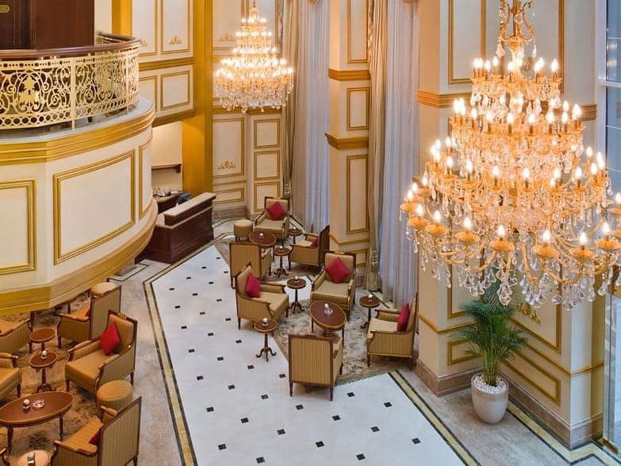 Lobby Café features tan chairs by small tables under large crystal chandeliers at Warwick Doha Hotel