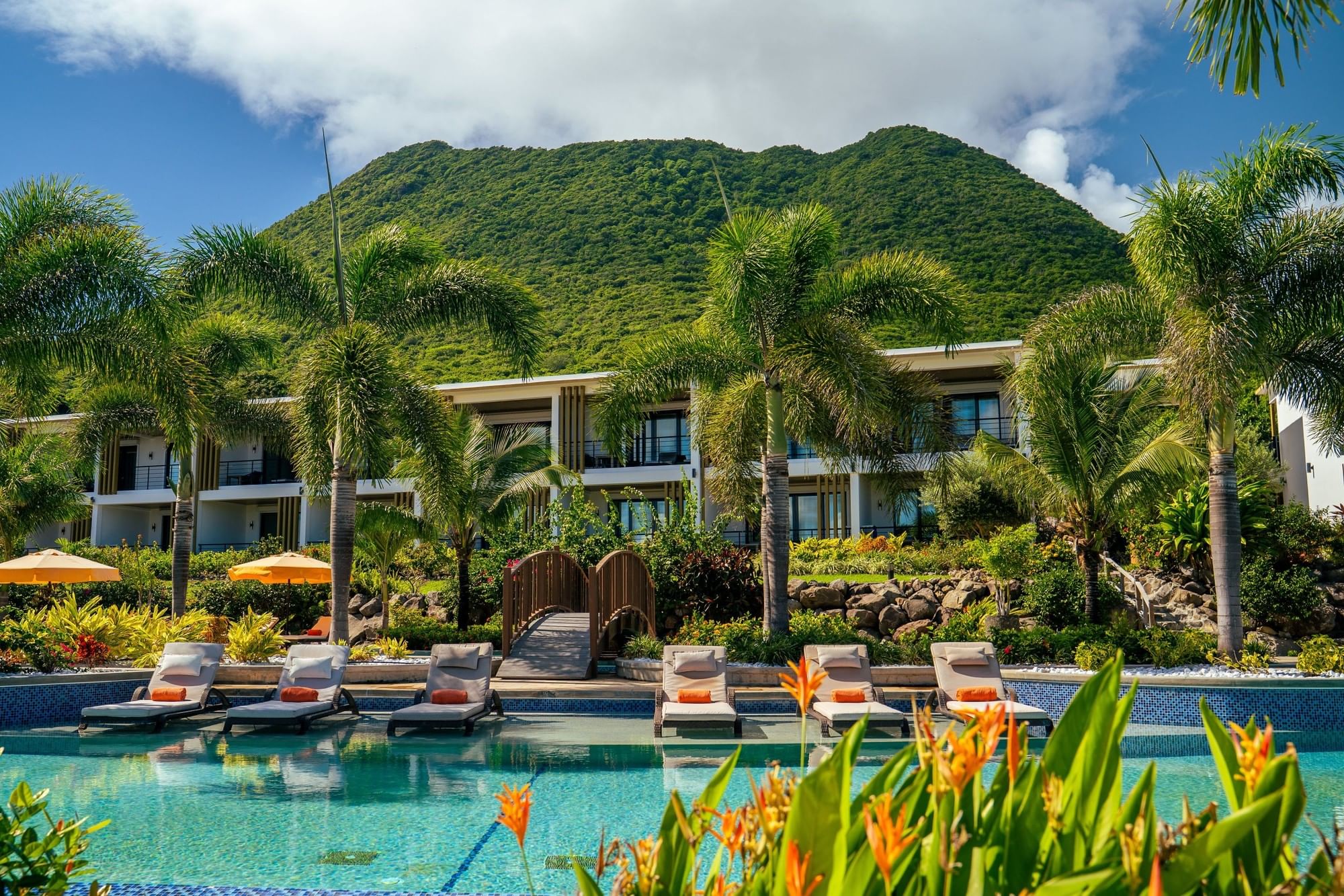 Outdoor swimming pool lined with sun loungers in front of a wooden bridge and a mountain at Golden Rock Resort