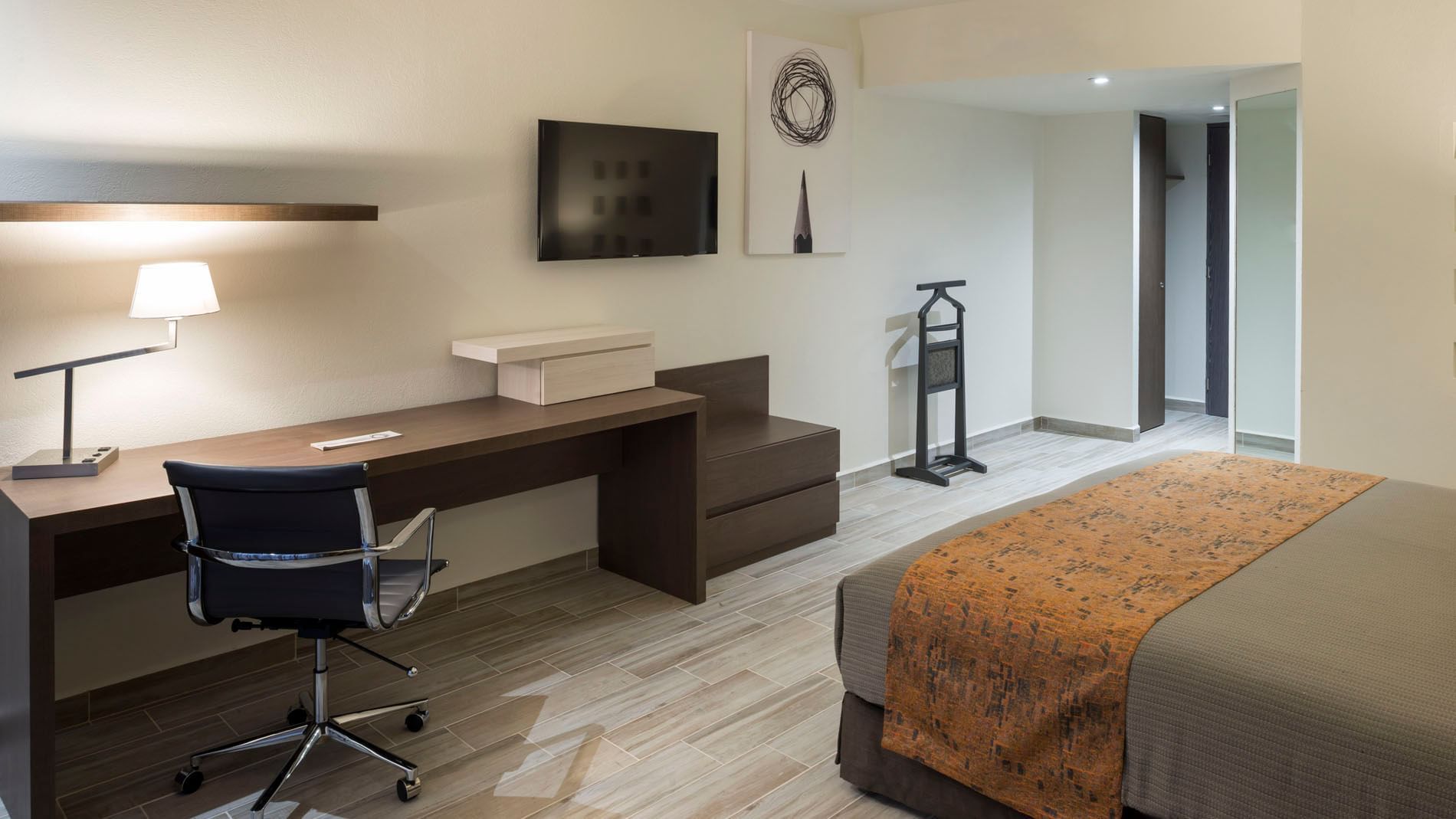 Work desk, dresser, and wall-mounted TV by the bed in the King Deluxe Room with wooden floors at Real Inn San Luis Potosi