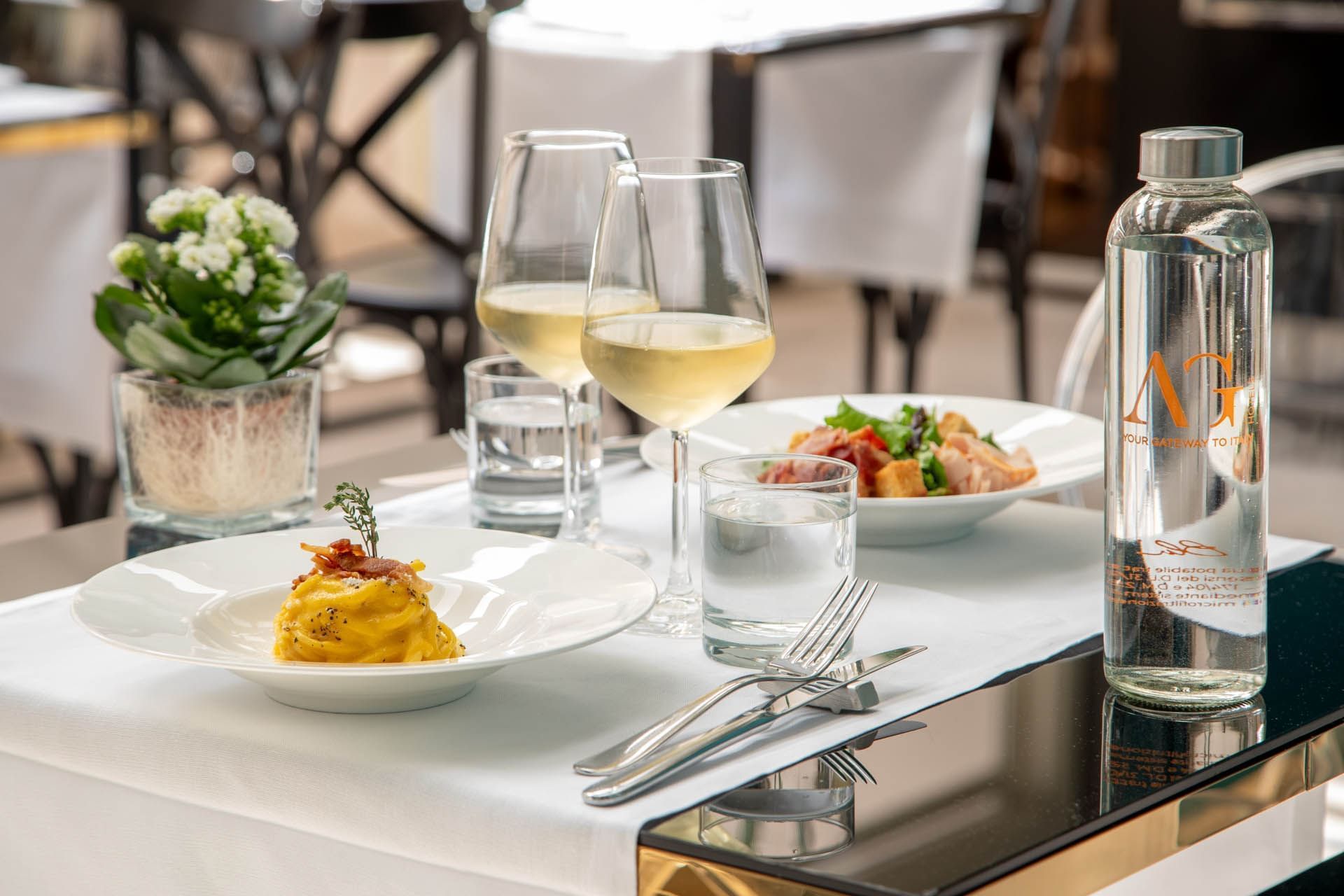 The Guardian Dehors dining table with pasta, salad, white wine, water, and a mini plant at The Guardian Hotel