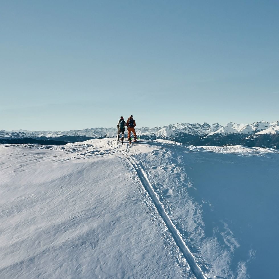 Due sciatori sulle piste innevate con vista sulle montagne innevate sotto un cielo blu.