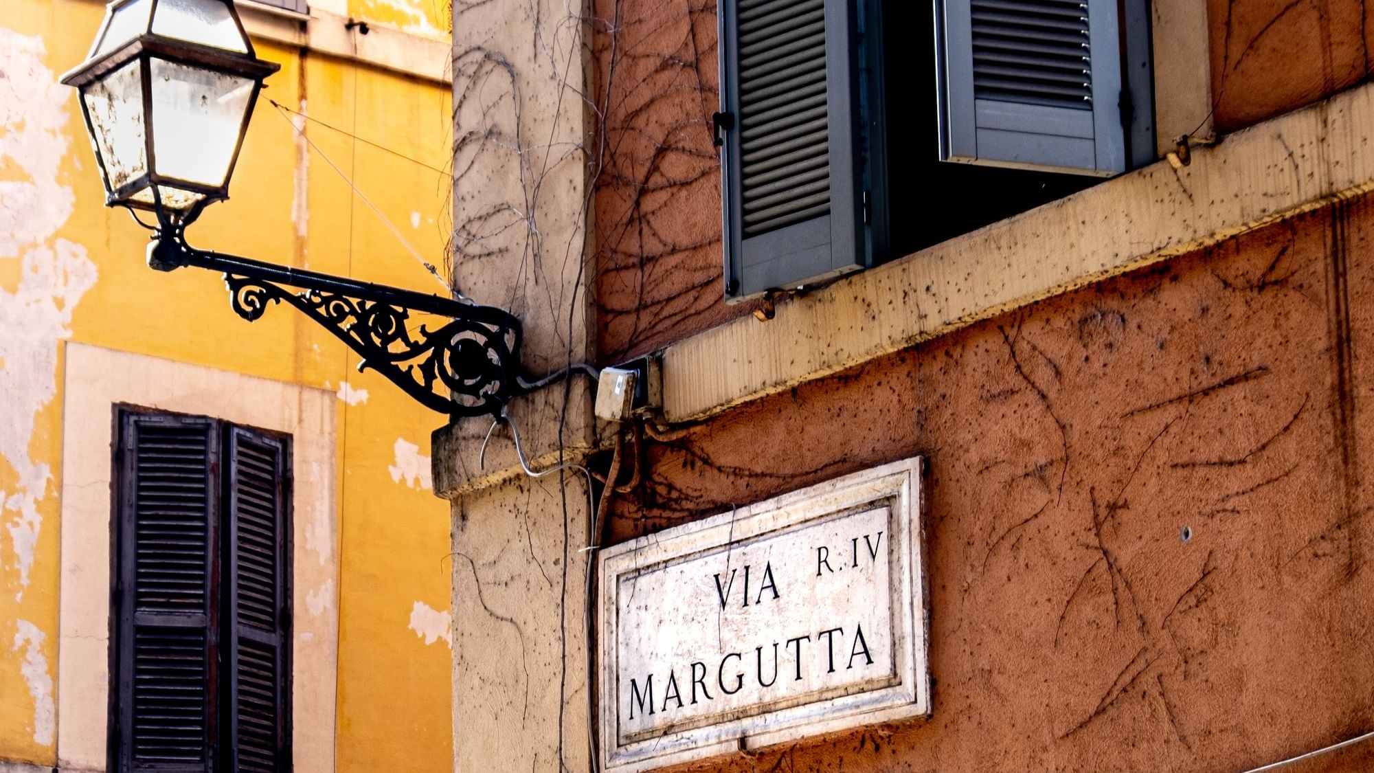 Ornate street lamp and Via Margutta sign on peeling wall near Rome Luxury Suites
