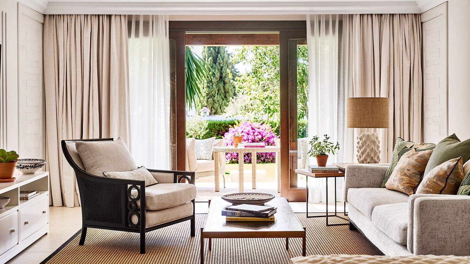 Living area with a sofa and armchair placed by glass doors that open to a garden patio at the Marbella Club 