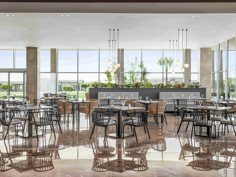 A large, modern restaurant with glass walls, tables, and chairs, and a reflective floor.