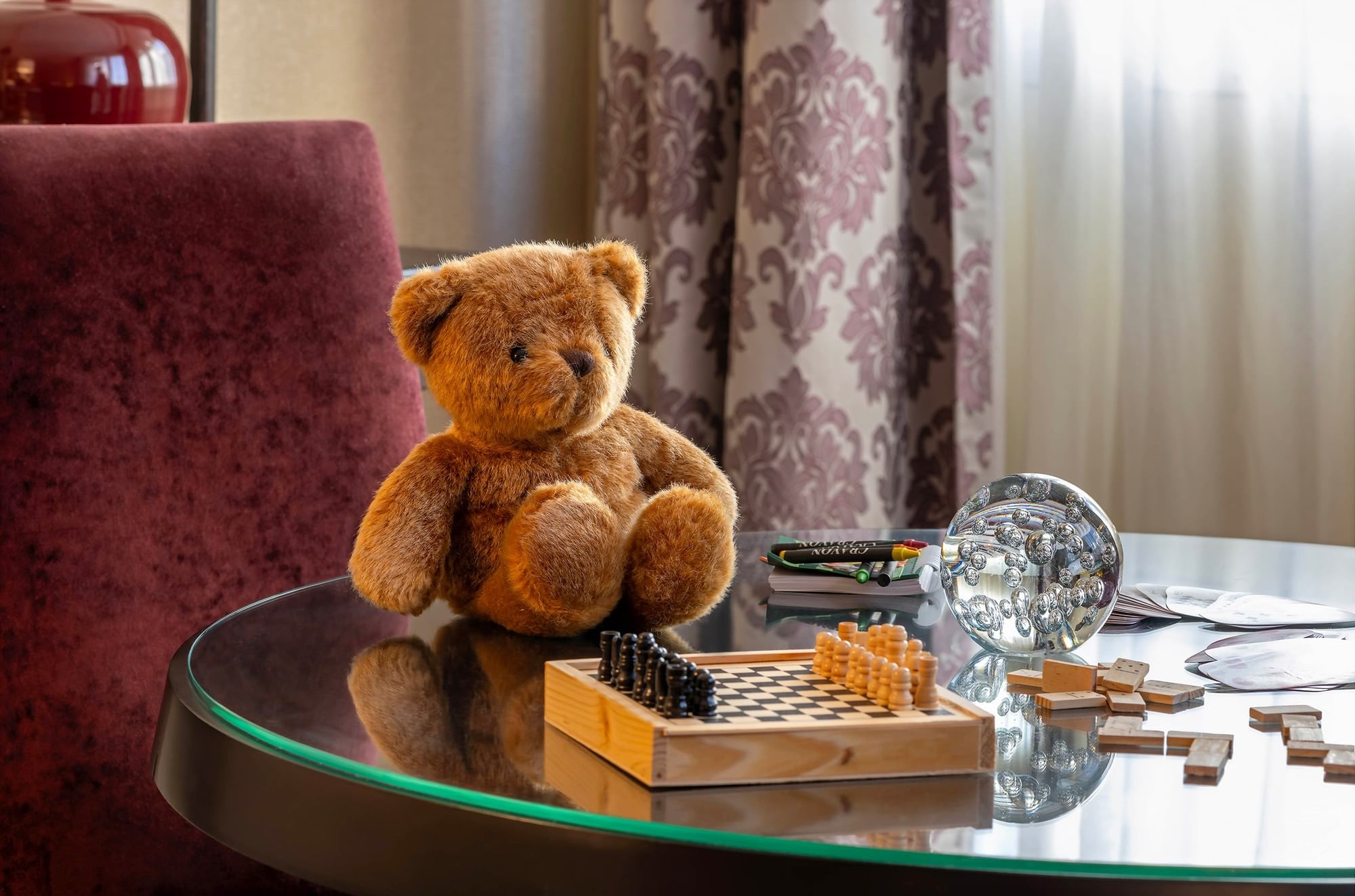 Teddy bear and chess set on a glass table by purple curtains in Family Room – Two Queen Beds at Warwick Paris Champs Elysées