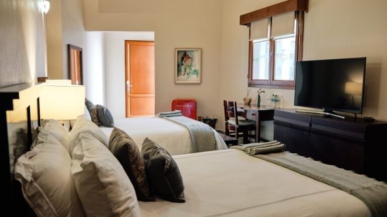 TV facing two beds and a work desk by the window in a room at the Curamoria Collection