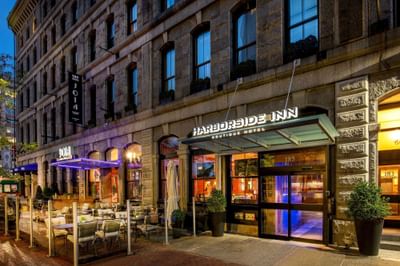 Granite historic exterior facade with glass entrance doors and a lit overhead sign at Harborside Inn Boston