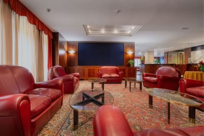 Hall featuring red leathered furniture, large screen & decorative rug at Hotel Crivi's in Milan