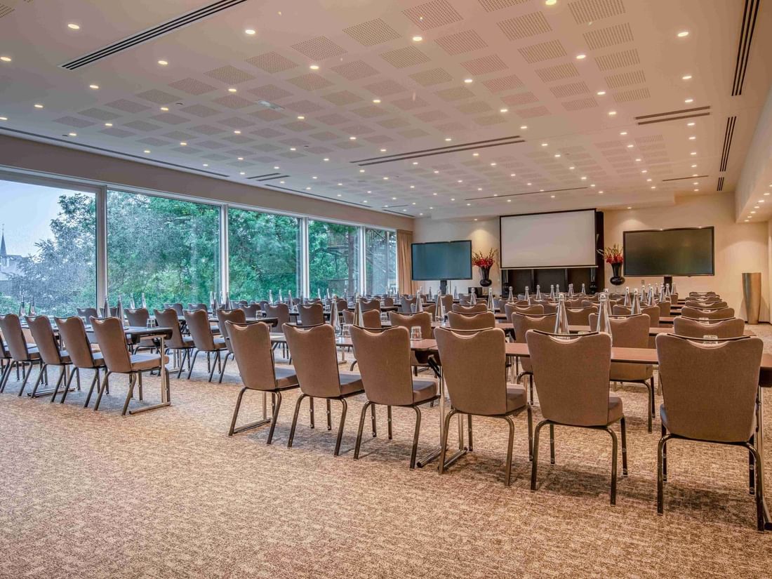 Park Ballroom with rows of chairs, large windows, screens, and water bottles on tables at The Hotel Brussels