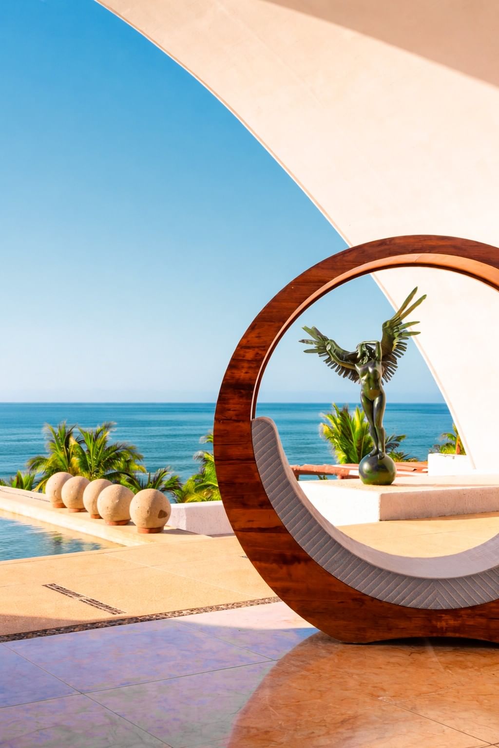 Circular wooden sculpture frames winged statue and ocean view at Marquis Los Cabos Resort & Spa