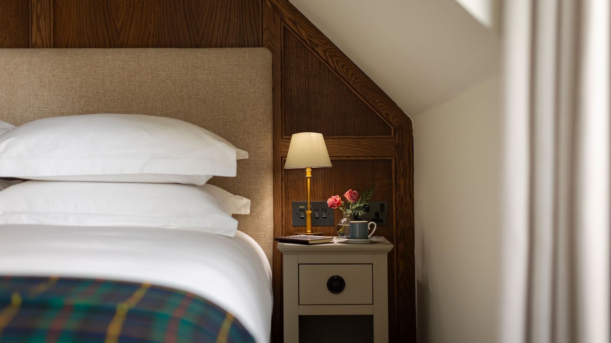 Bedside table, with a lamp, book, and flowers, beside a bed in Signature Accessible at Seaton House