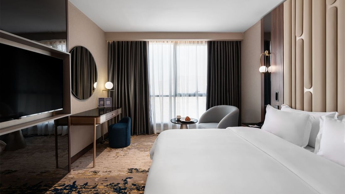 TV with work desk facing the bed & couch by the window in Deluxe Room at Warwick Al Taif Hotel