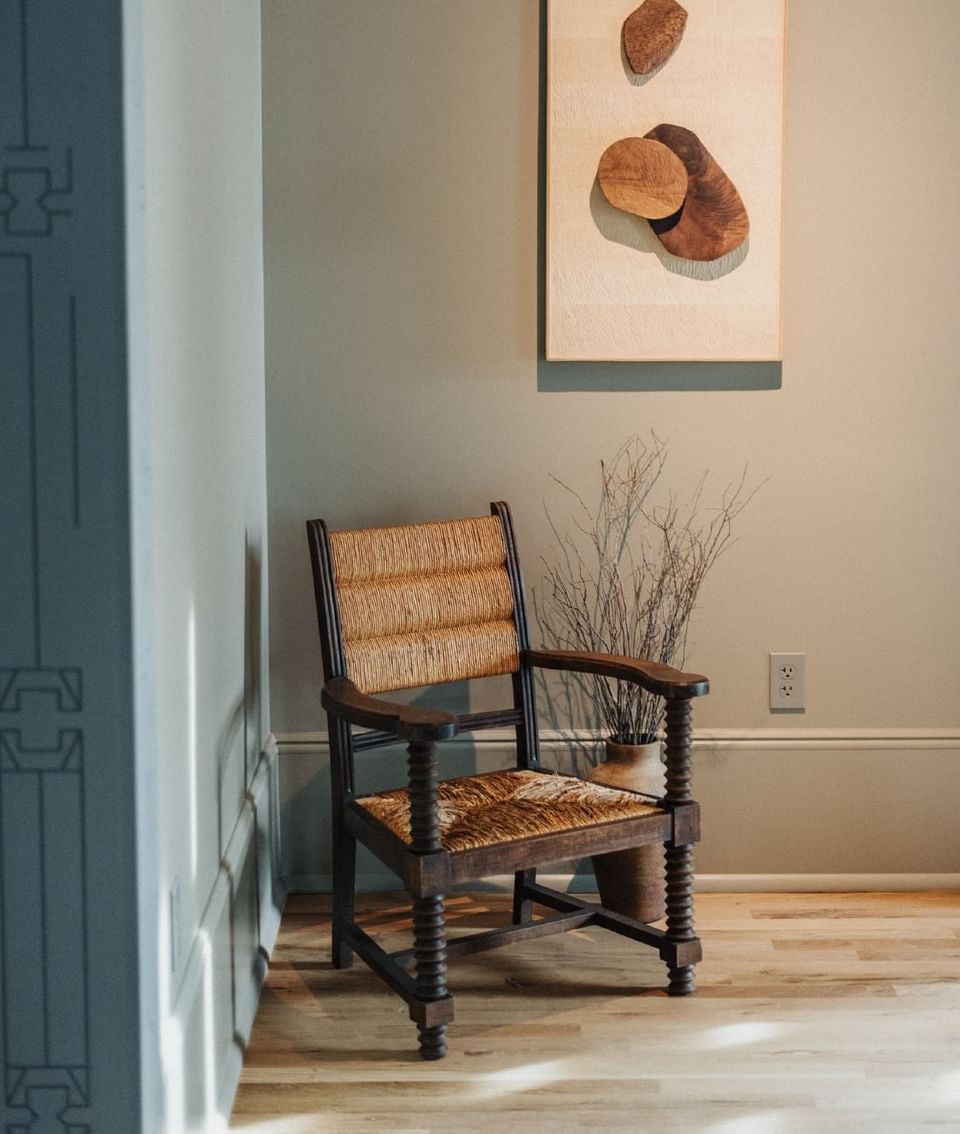 Wooden armchair with wicker seat beside a wall with abstract art at The Stonebreaker Hotel