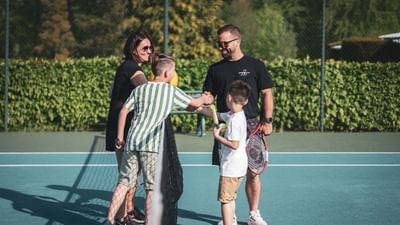 A family of four, two adults and two children, shakes hands on a tennis court.