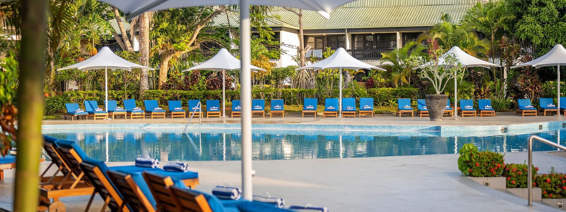 Blue lounge chairs under umbrellas by a swimming pool at The Naviti Resort - Fiji in Korolevu