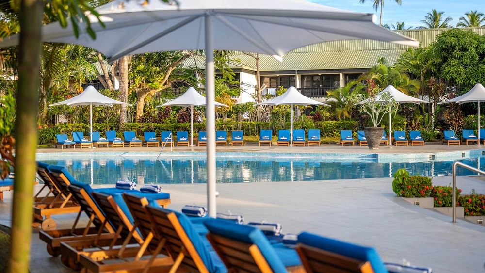 Blue lounge chairs under umbrellas by a swimming pool at The Naviti Resort - Fiji in Korolevu.