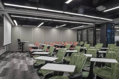 Classroom with green and orange chairs, white desks, and a projector screen in Rooms A B & C at Hotel Nodo