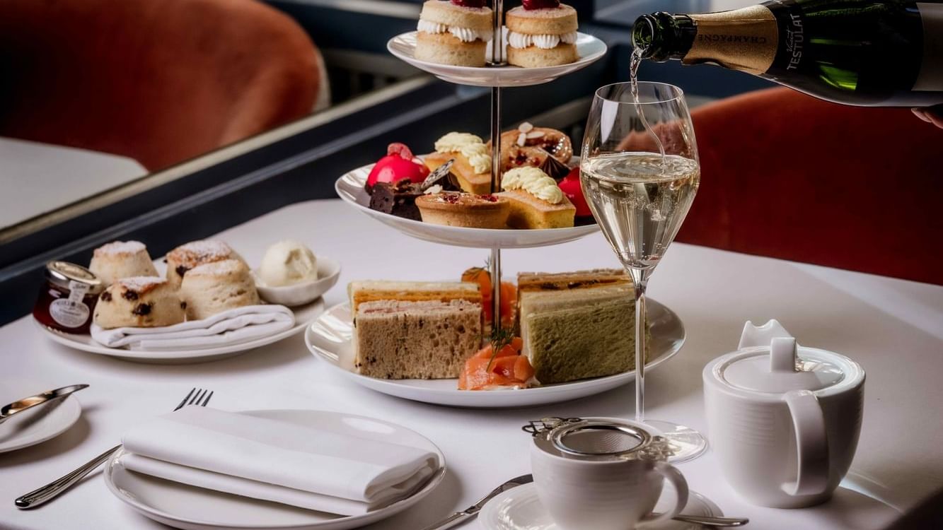 Champagne is poured into a glass on a table set with desserts and tea cups at Warwick Hotels and Resorts