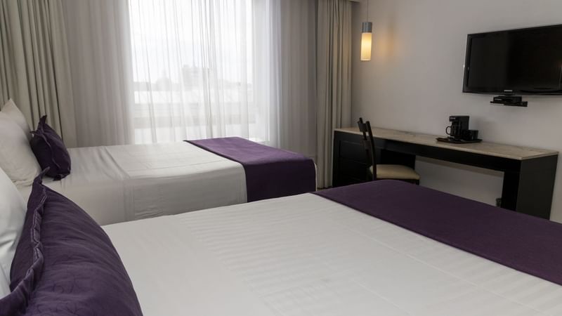 Two beds, work desk, coffee maker & TV in a room at Gamma Puebla Senorial Centro