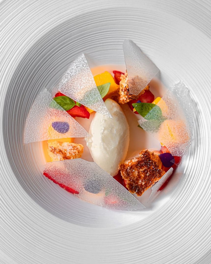 Arranged dessert with fruits, ice cream, and delicate sugar shards on a white plate at The Kitchens