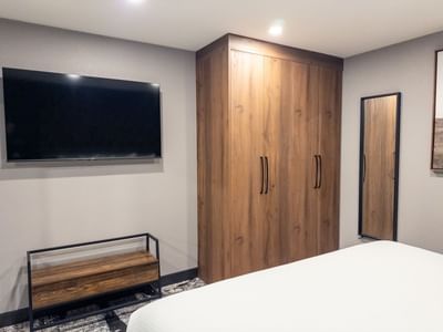 Modern bedroom with flat-screen TV, wooden armoire, and white bed at Carriage House Hotel & Conference Centre.