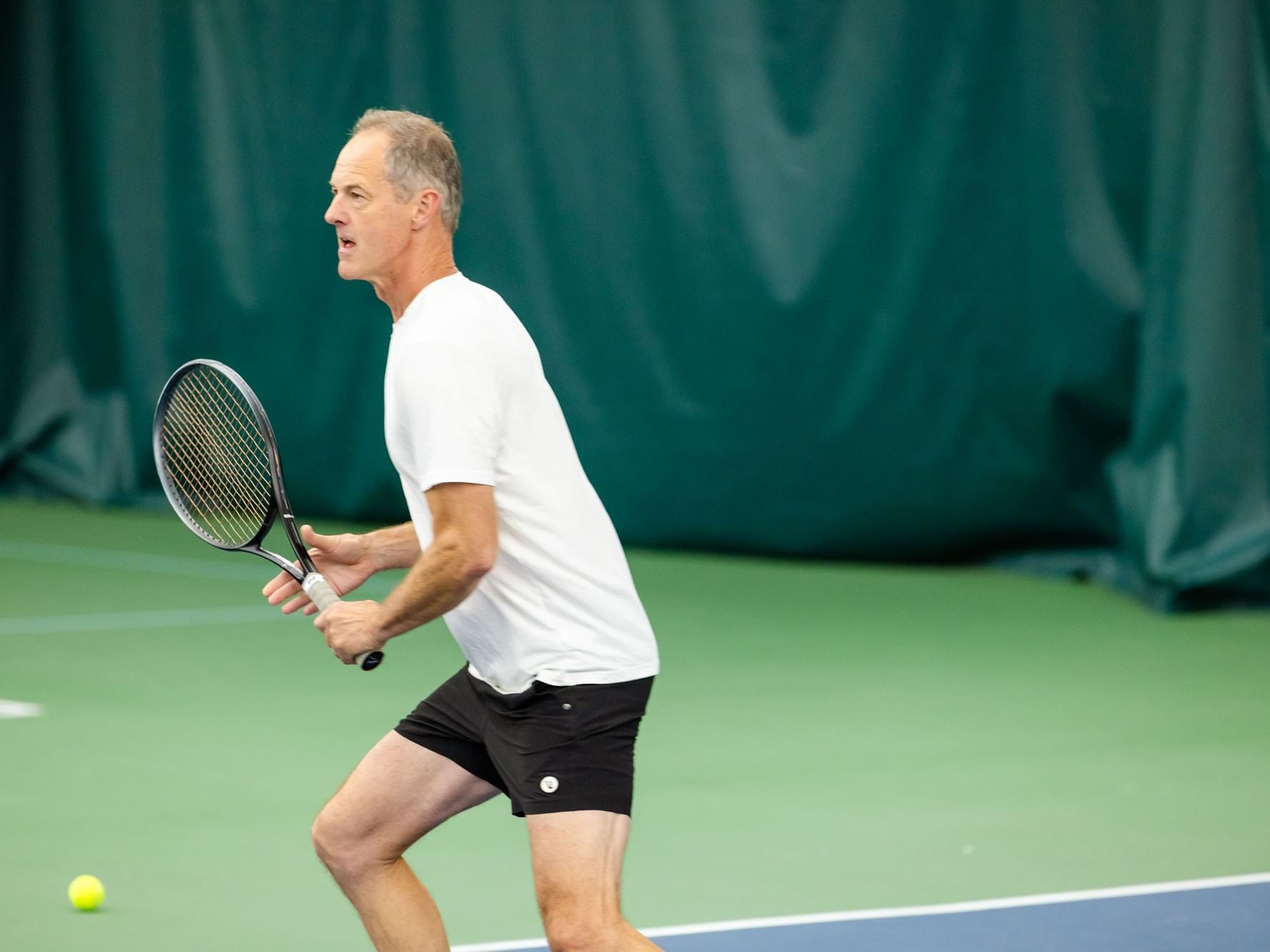 Man playing tennis with a tennis racket and ball on a tennis court.