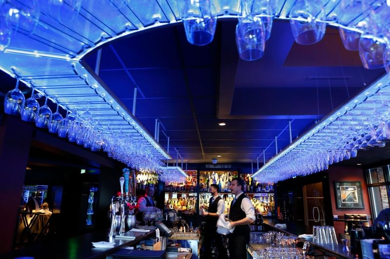Bartenders working under a bright blue ceiling with hanging wine glasses in Chandler's Steakhouse at Hotel 43 Boise
