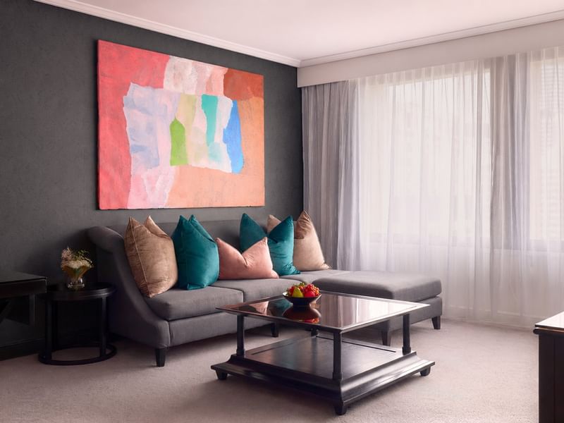 Living area of Signature Suite with chaise lounge, pillows, painting, and glass table at Sofitel Brisbane Central.