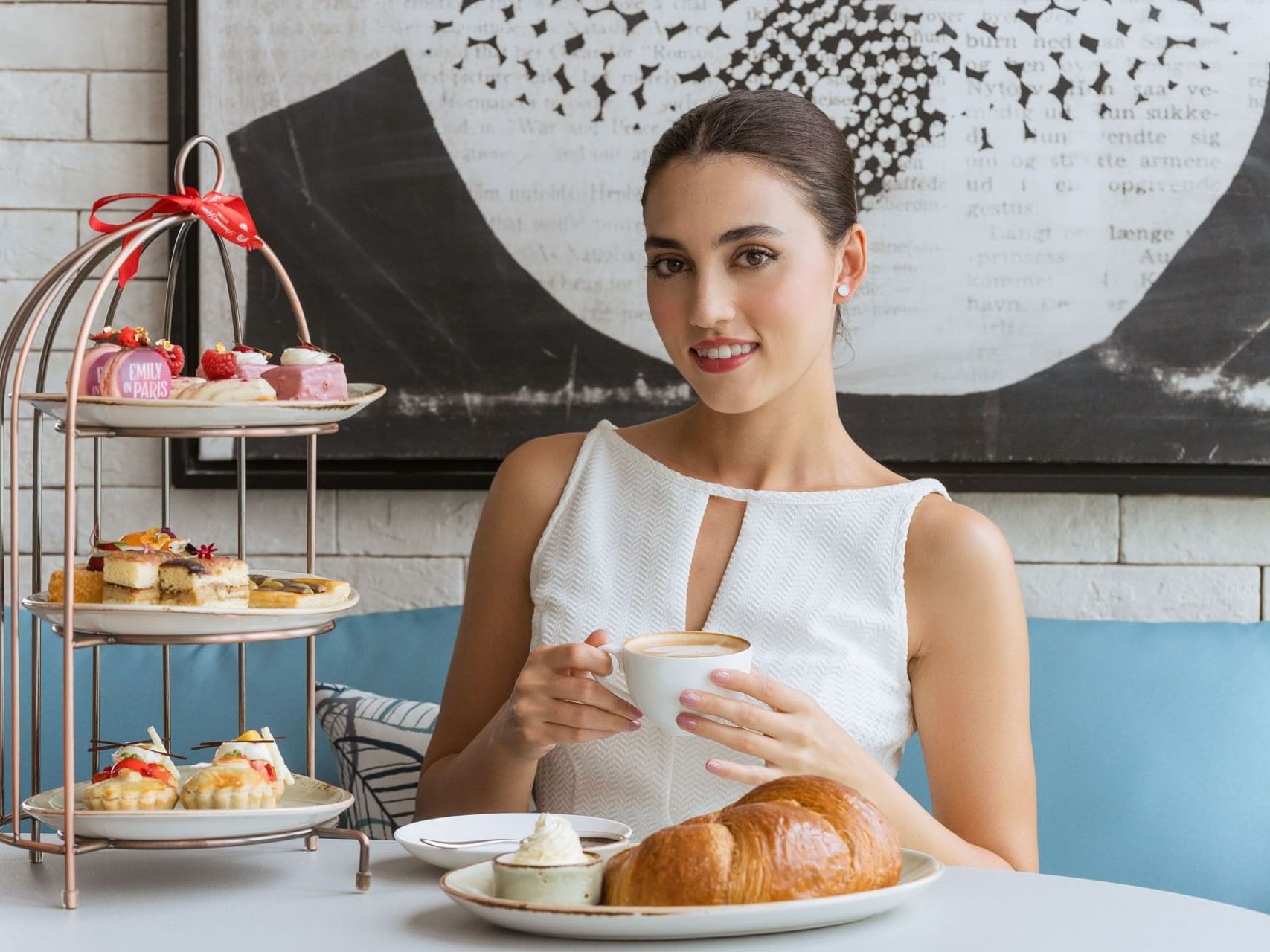 Woman in a white top enjoying coffee alongside croissants during the Emily in Paris Afternoon Tea at Malibu Sky Lounge & Bar