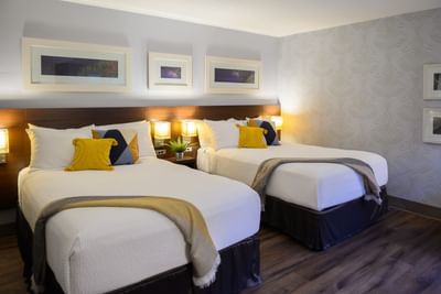 Two comfortable queen beds with yellow accent pillows and warm lit headboard lamps in a guestroom at Rodd Moncton