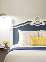 Yellow patterned pillow on a bed by a floating nightstand under a reading lamp in Suite at Warwick San Francisco