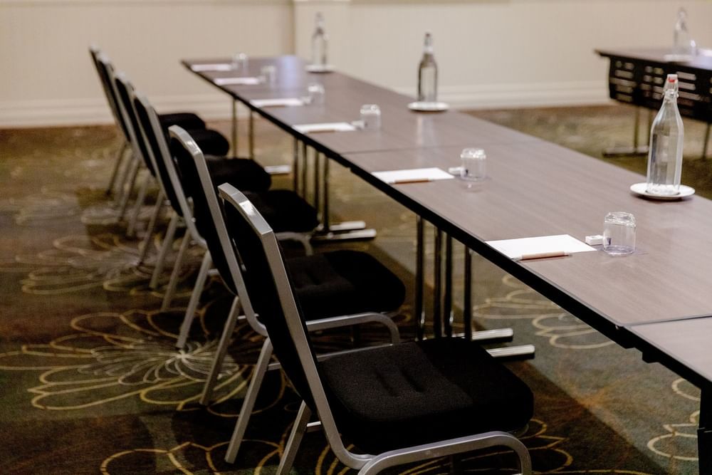 Long conference table with notepads, pens, and water bottles, flanked by rows of black chairs.