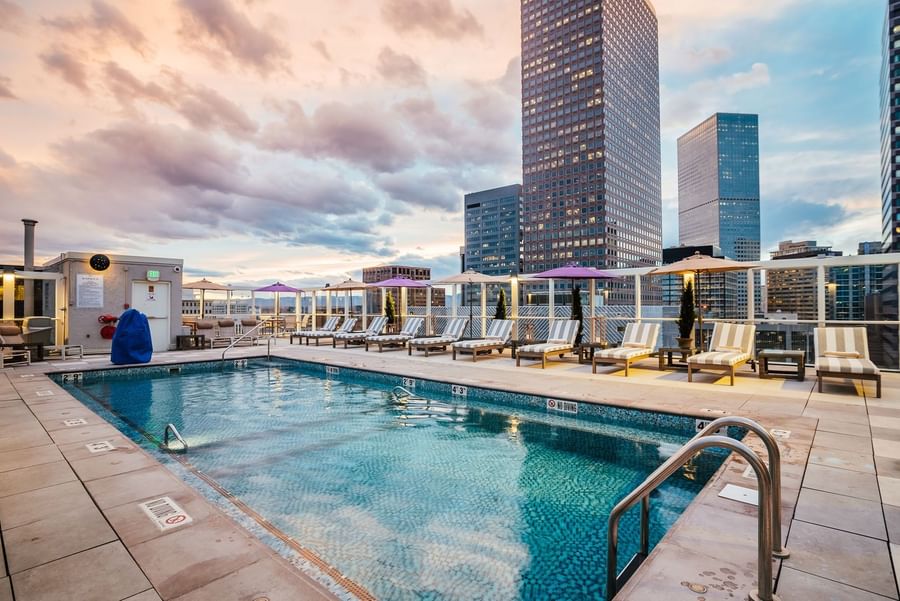 Striped lounge chairs by a blue pool under a cloudy sky near city skyscrapers in Poolside at Warwick Denver