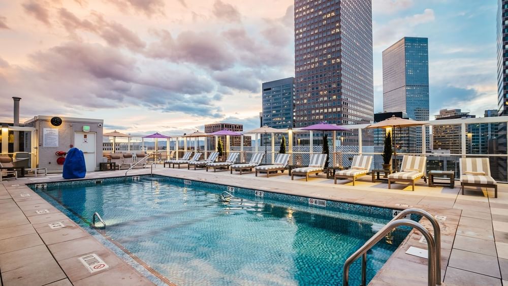 Striped lounge chairs by a blue pool under a cloudy sky near city skyscrapers in Poolside at Warwick Denver