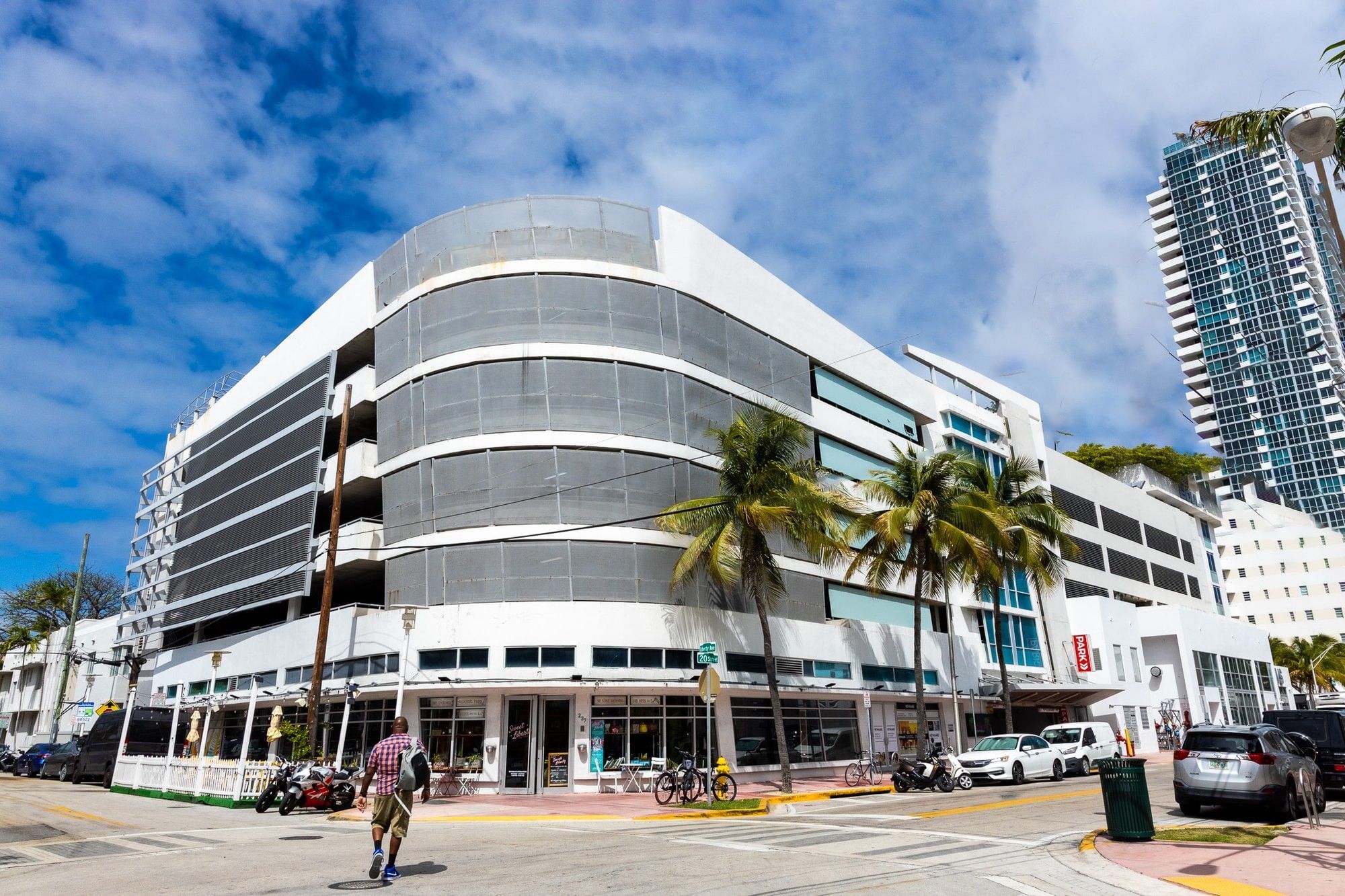 A white, multi-story building with a curved facade and palm trees in front of it.