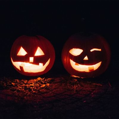 Two carved jack-o'-lanterns sit side-by-side in the dark at Falkensteiner Hotel Sonnenalpe