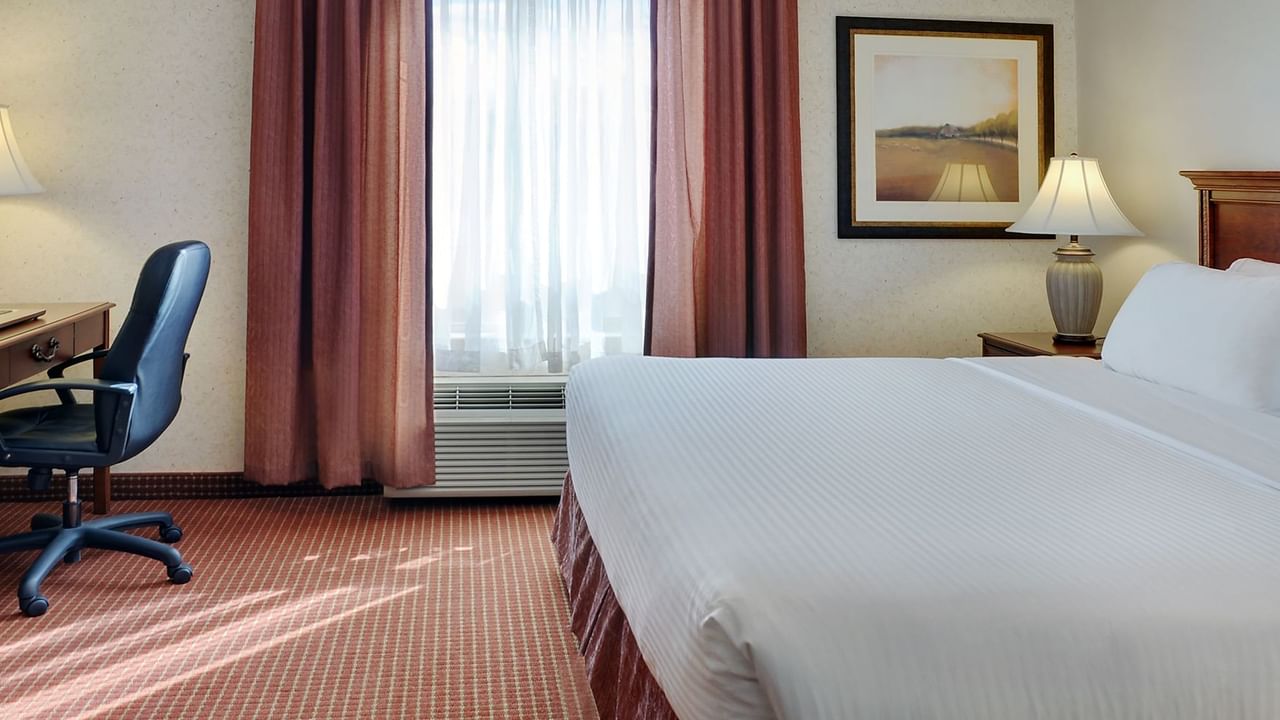 Hotel suite with king bed, curtains, lamp, working desk, and window