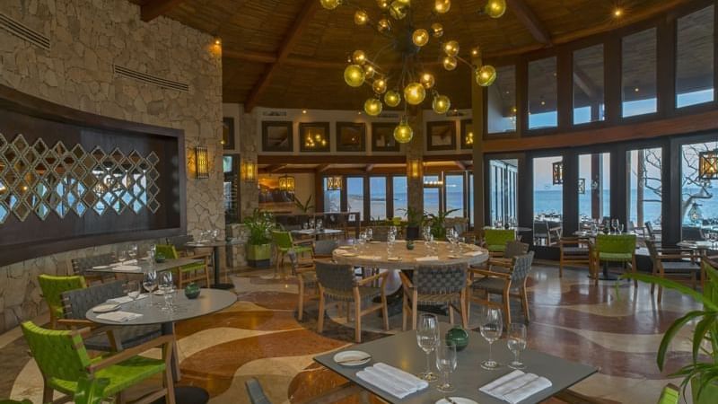 Comedor de De Cortez Grill House con sillas verdes, mesas redondas junto a los ventanales con vista al mar en Hacienda Del Mar Los Cabos
