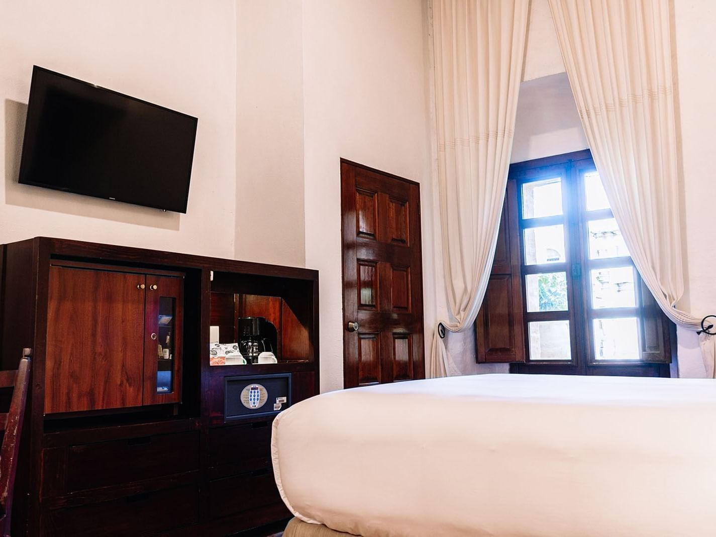 Wall-mounted TV, side cupboard, and coffee maker facing the bed in Queen Novicia Suite at Quinta Real Oaxaca