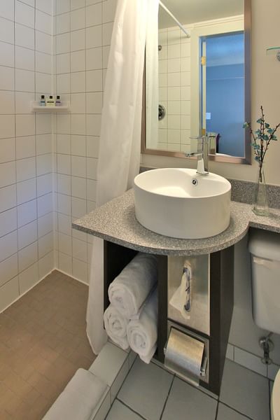White vessel sink on a granite vanity with rolled towels underneath in a clean hotel suite bathroom at Rodd Moncton